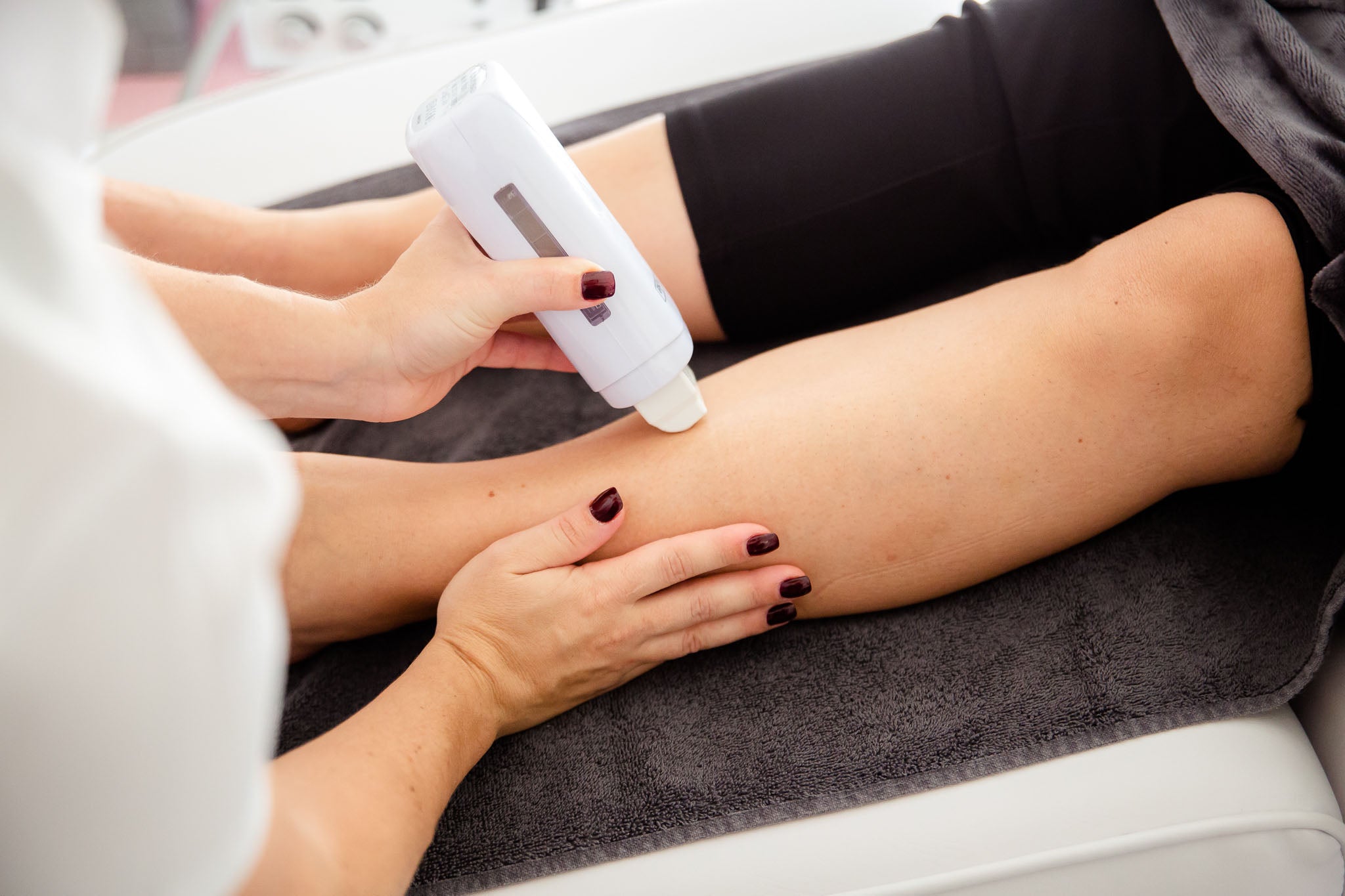 Kosmetikerin bei der professionellen Haarentfernung am Bein einer Kundin mit einem modernen Gerät – hygienische Behandlung im Kosmetikstudio